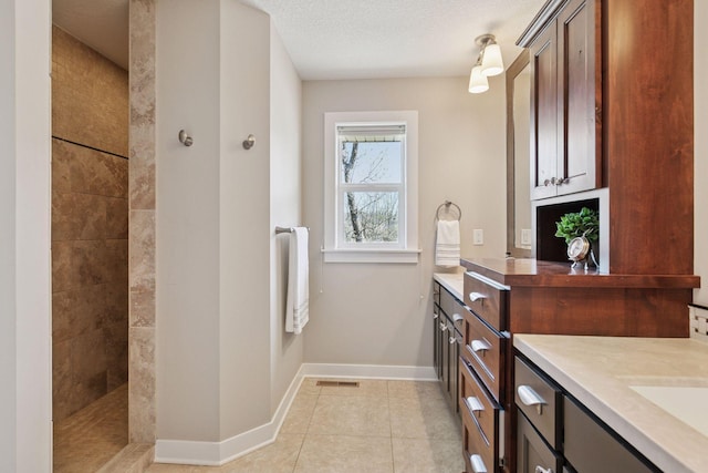 bathroom featuring walk in shower, vanity, tile patterned floors, baseboards, and visible vents