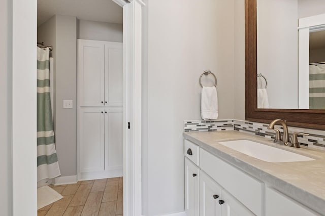 full bath with vanity, baseboards, wood finished floors, and tasteful backsplash