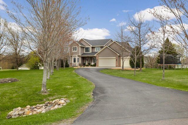 view of front of house with a garage, a front lawn, brick siding, a trampoline, and driveway
