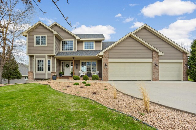 traditional-style house featuring covered porch, brick siding, a front lawn, concrete driveway, and an attached garage