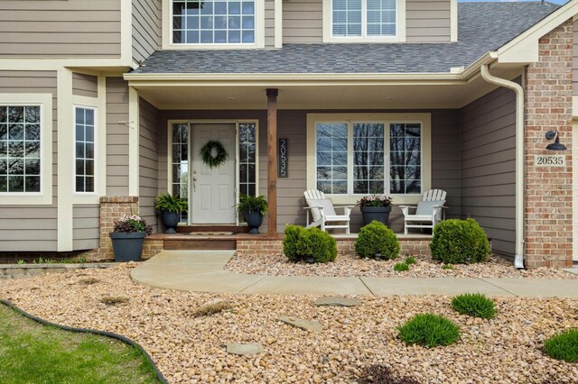 property entrance featuring a porch, brick siding, and a shingled roof