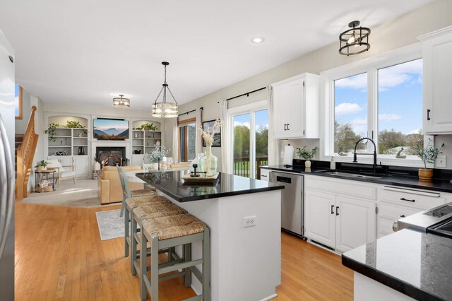 kitchen with a kitchen island, dark countertops, light wood-type flooring, dishwasher, and a sink