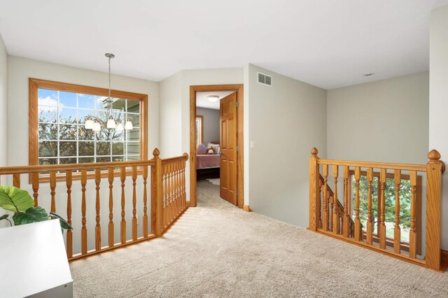 hallway featuring carpet floors, an upstairs landing, an inviting chandelier, and visible vents