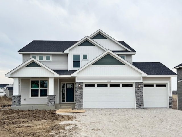 craftsman-style home with a garage, gravel driveway, stone siding, and a shingled roof