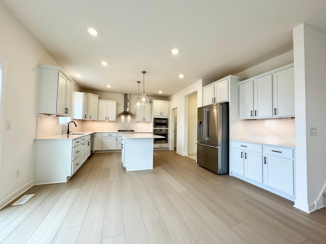 kitchen with a center island, light countertops, light wood finished floors, stainless steel appliances, and wall chimney exhaust hood