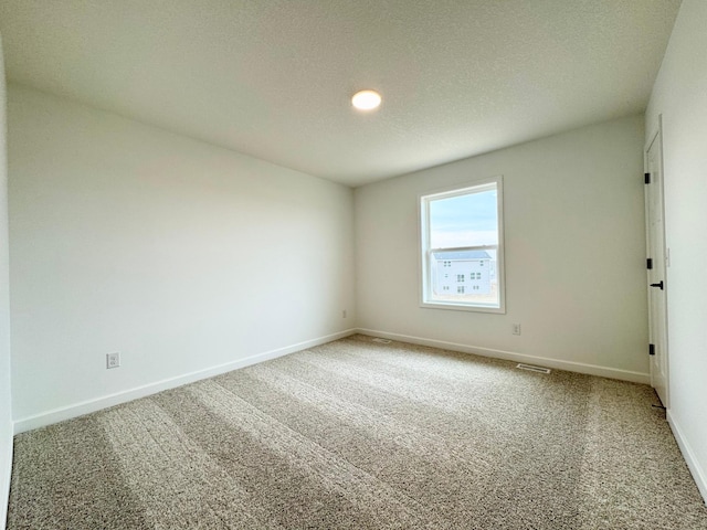 carpeted spare room with a textured ceiling, baseboards, and visible vents