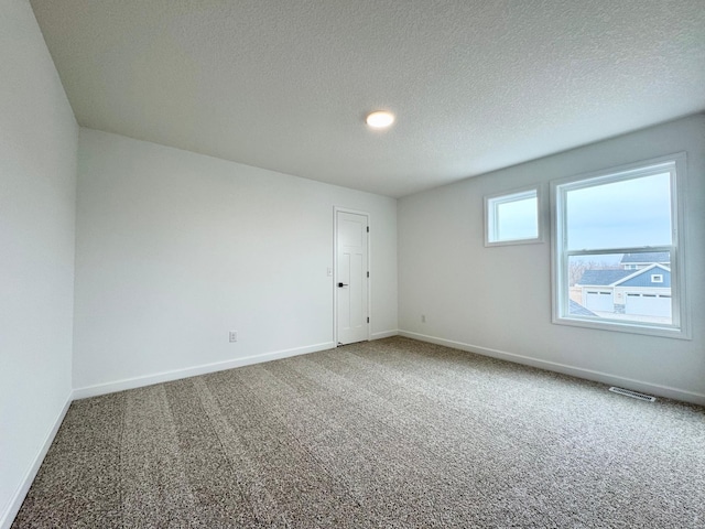 carpeted spare room with a textured ceiling, baseboards, and visible vents