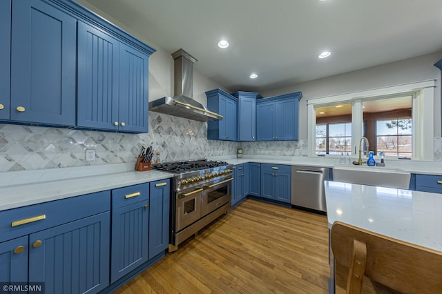 509 Superior Ave, Crosby, MN 56441 - kitchen with wall chimney range hood, appliances with stainless steel finishes, a sink, blue cabinetry, and wood finished floors