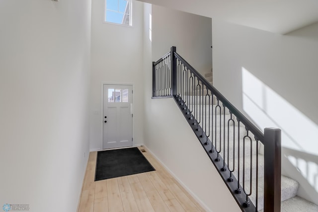 foyer entrance with a healthy amount of sunlight, baseboards, wood finished floors, and a towering ceiling