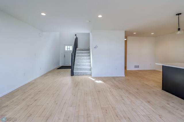 unfurnished living room with visible vents, stairs, light wood finished floors, and baseboards
