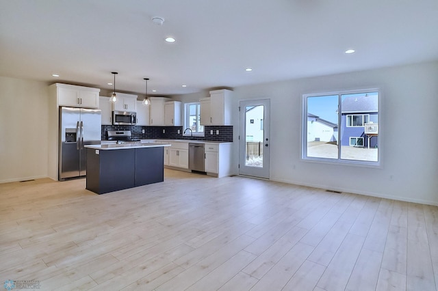 kitchen featuring light wood-style floors, a center island, a sink, appliances with stainless steel finishes, and backsplash