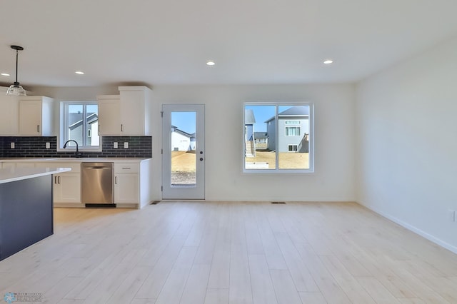 kitchen with stainless steel dishwasher, a sink, white cabinetry, and decorative backsplash