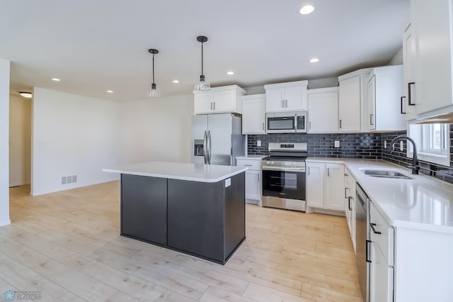 kitchen with visible vents, a kitchen island, light countertops, a sink, and stainless steel appliances