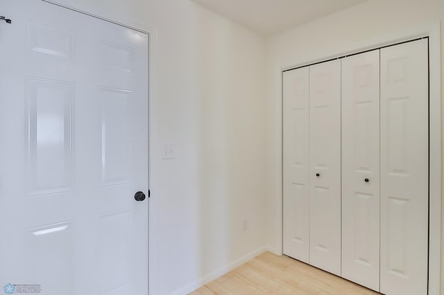 unfurnished bedroom featuring light wood-type flooring, baseboards, and a closet