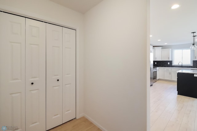 hall featuring recessed lighting, baseboards, a sink, and light wood-style floors