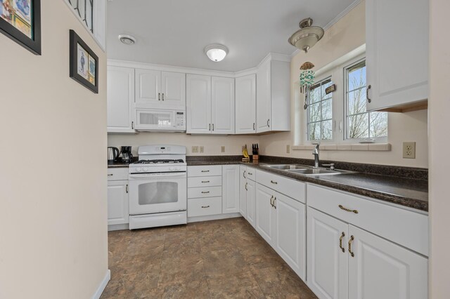 kitchen with dark countertops, a sink, white appliances, stone finish floor, and white cabinetry