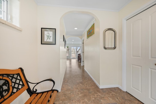 hallway featuring ornamental molding, baseboards, stone finish floor, recessed lighting, and arched walkways
