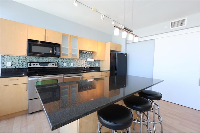 kitchen featuring visible vents, light brown cabinetry, a breakfast bar, a sink, and black appliances