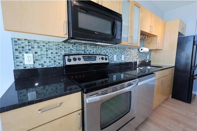 kitchen featuring light wood-type flooring, tasteful backsplash, a sink, dark stone countertops, and black appliances