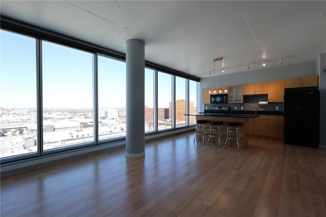 kitchen featuring decorative backsplash, wood finished floors, a breakfast bar, dark countertops, and black appliances