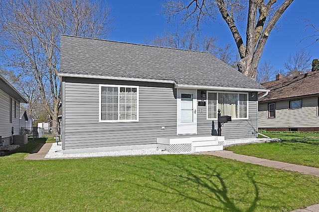 bungalow with a shingled roof, a front lawn, central AC, and fence