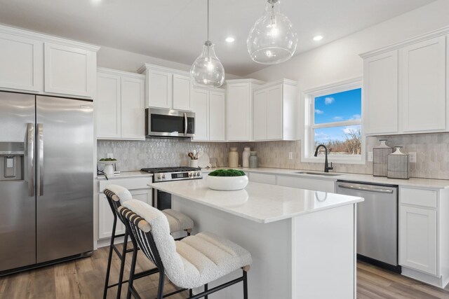 kitchen featuring stainless steel appliances, white cabinetry, a sink, and a center island