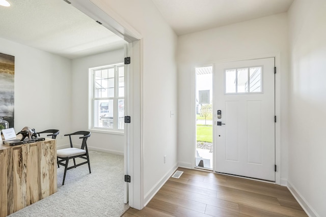 entrance foyer with visible vents, baseboards, wood finished floors, and a healthy amount of sunlight