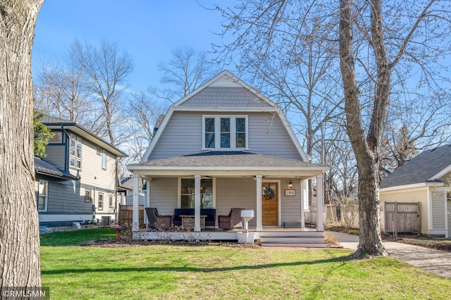 colonial inspired home with covered porch, roof with shingles, a front yard, and a gambrel roof