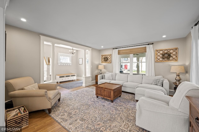 living area featuring wood finished floors, baseboards, recessed lighting, ornate columns, and a notable chandelier