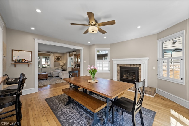 dining space featuring light wood-type flooring, a glass covered fireplace, ceiling fan, and baseboards