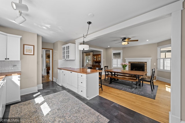 kitchen featuring a fireplace, backsplash, butcher block countertops, and white cabinetry