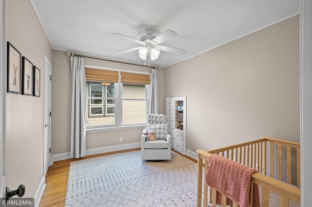 bedroom featuring crown molding, baseboards, a crib, a ceiling fan, and light wood finished floors