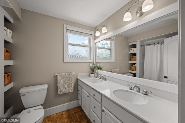 bathroom with double vanity, toilet, baseboards, and a sink