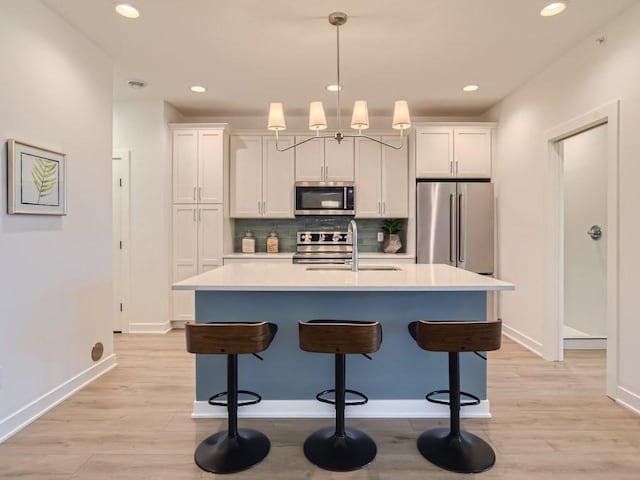 kitchen featuring appliances with stainless steel finishes, a sink, light wood-style floors, an island with sink, and decorative backsplash