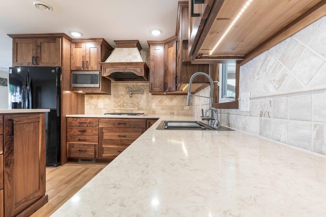 22694 Coney Island Dr, Clitherall, MN 56524 - kitchen featuring appliances with stainless steel finishes, premium range hood, a sink, light stone counters, and brown cabinetry