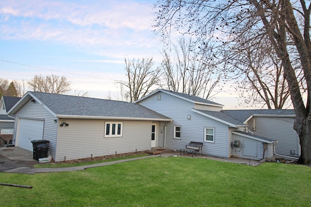 back of property with a lawn, a shingled roof, a garage, and concrete driveway