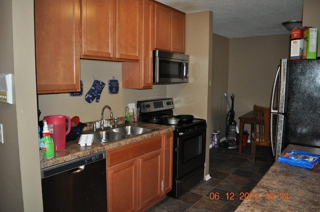 kitchen featuring a textured ceiling, brown cabinets, a sink, stone finish flooring, and stainless steel appliances