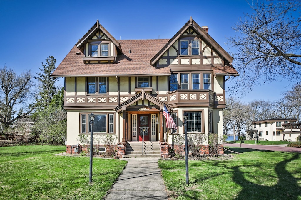 tudor-style house with roof with shingles, stucco siding, and a front yard