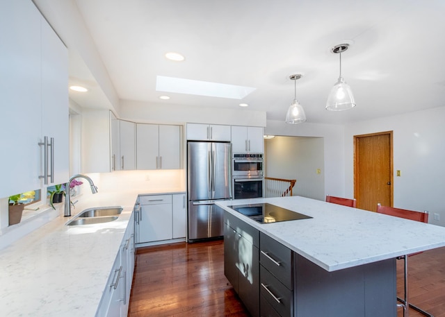 kitchen with appliances with stainless steel finishes, a skylight, white cabinets, a sink, and a kitchen bar