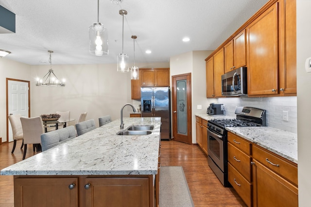 kitchen with wood finished floors, brown cabinets, a sink, backsplash, and stainless steel appliances