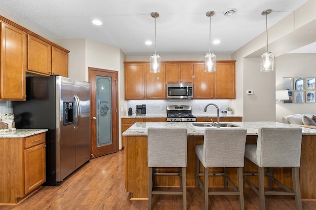 kitchen with a sink, appliances with stainless steel finishes, brown cabinetry, and light wood finished floors