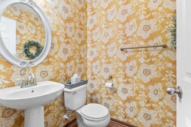 bathroom with baseboards, a sink, toilet, and wallpapered walls