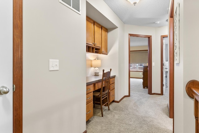office with a textured ceiling, light colored carpet, visible vents, built in study area, and baseboards