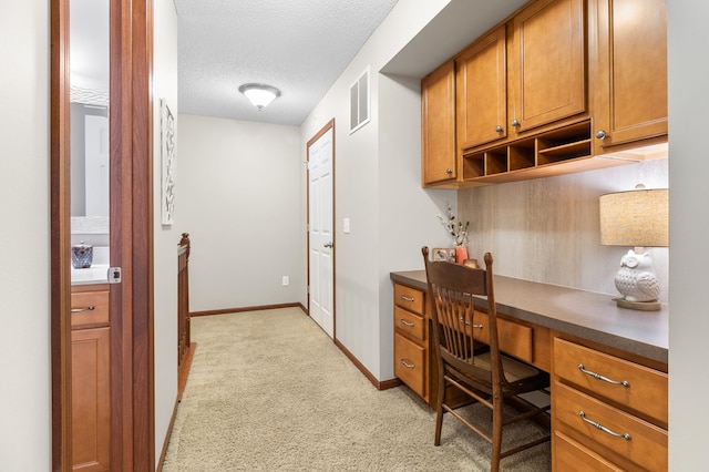 office featuring a textured ceiling, visible vents, light colored carpet, built in study area, and baseboards