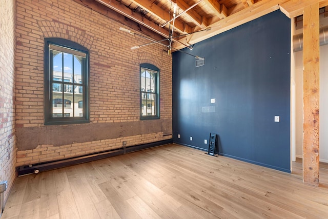 empty room featuring brick wall, hardwood / wood-style flooring, wood ceiling, beamed ceiling, and baseboards