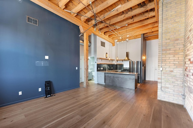 kitchen featuring dark wood-style flooring, white cabinets, a towering ceiling, beam ceiling, and brick wall