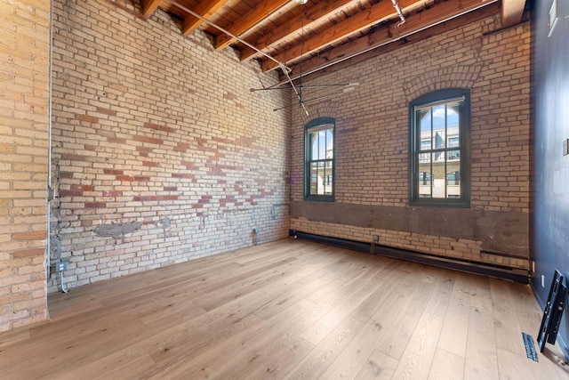 empty room featuring brick wall, beamed ceiling, wood ceiling, wood finished floors, and a high ceiling