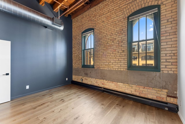 spare room with brick wall, beam ceiling, wood ceiling, wood finished floors, and a high ceiling