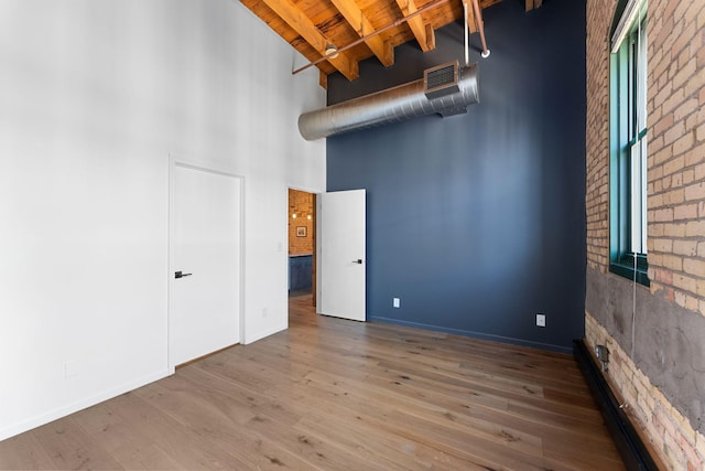 spare room with a towering ceiling, beam ceiling, wooden ceiling, wood finished floors, and brick wall