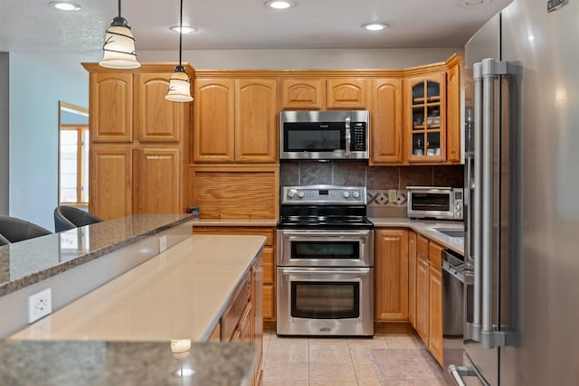 2606 Hulett Ct, Faribault, MN 55021 - kitchen with appliances with stainless steel finishes, glass insert cabinets, backsplash, light tile patterned floors, and pendant lighting